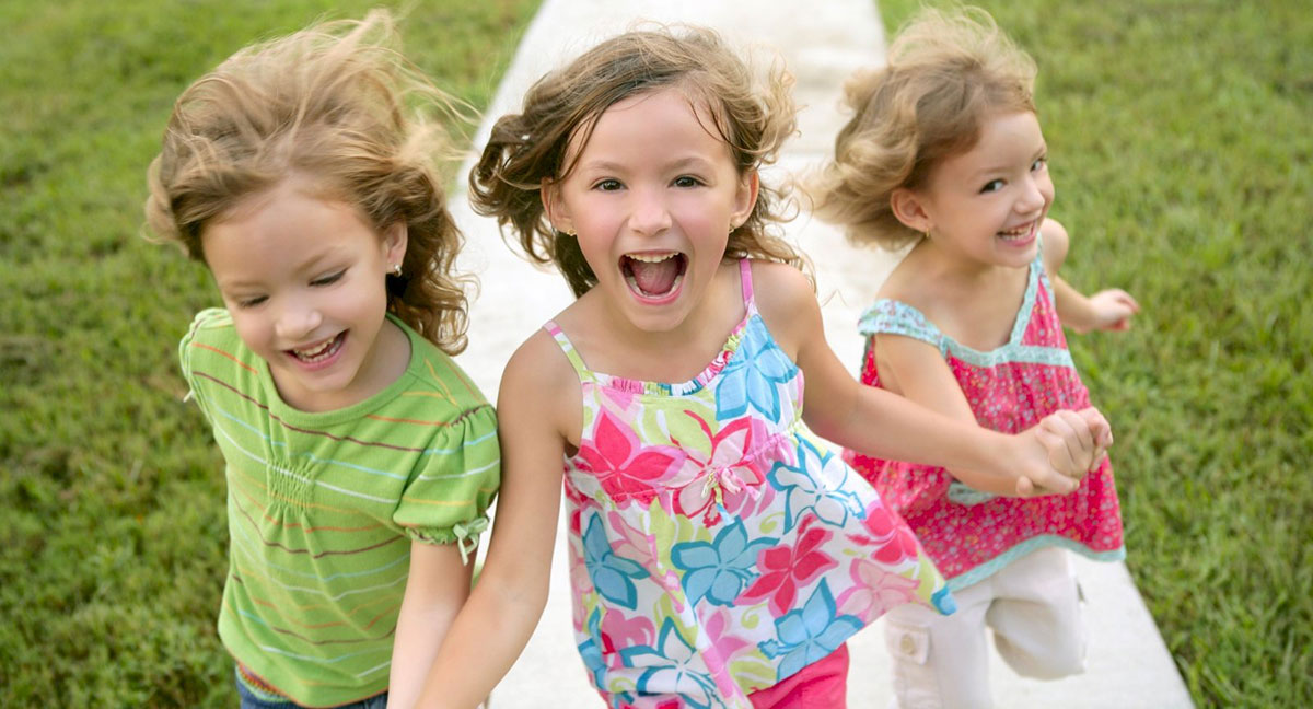 Drie kinderen kijken lachend de camera in.